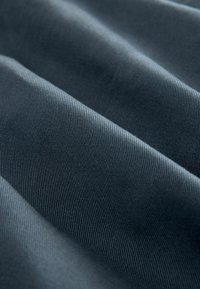 Strukturierter Stoff in Dunkelblau mit diagonalem Rippenmuster. Die Oberfläche wirkt weich mit einem subtilen Glanz und zeigt wellige Falten und Tiefe.