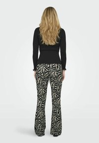 Svart långärmad topp tillsammans med utsvängda byxor med zebra-mönster i beige och svart, som visar en mjuk, texturerad tyg.