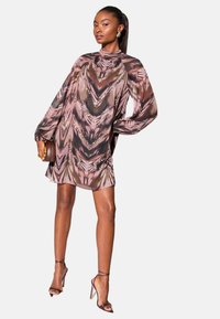 Rochie transparentă, multicoloră, cu un model abstract în nuanțe de mov și maro, cu mâneci lungi, guler înalt și siluetă fluidă. Asortată cu pantofi cu toc subțire.