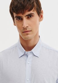 Jasnoniebieska, zapinana na guziki koszula z teksturowanej tkaniny, z klasycznym kołnierzykiem, gładkimi guzikami i bez widocznych wzorów czy akcentów.