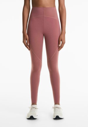Hoogwaardige, lichtroze leggings met een gladde textuur, voorzien van contrasterende naden en een strakke pasvorm. Gepaard met witte sportschoenen.