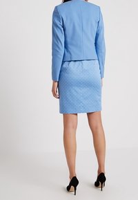 Light blue tailored jacket and polka dot pencil skirt, both featuring a smooth fabric texture. High-heeled black shoes complete the outfit.