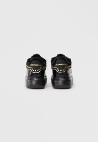 Sorte sneakers med en blank lærfinish, med en faux fur krage og gullnagle, merket med "KARL LAGERFELD" på hælen.