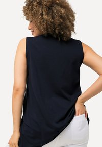 Top senza maniche di colore blu navy realizzato in tessuto morbido, con una vestibilità rilassata e orlo curvo. Indossato con pantaloni bianchi, mette in mostra un look casual.
