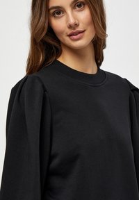 Črna majica s kapuco iz mehkega blaga, z okroglim izrezom in izrazitimi napihnjenimi rokavi, z gladkim, teksturiranim zaključkom.