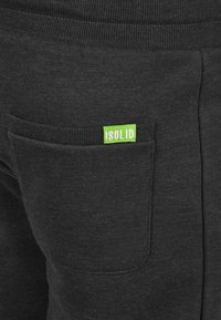 Black sweatpants featuring a ribbed waistband, side pocket, and a small green logo tag labeled "!SOLID" on the pocket.
