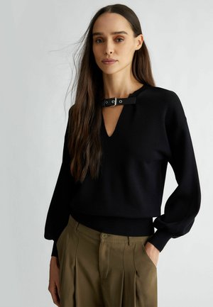 Maglione nero lavorato a maglia con scollatura a V e dettagli in finta pelle sulla collana. Presenta maniche lunghe a palloncino e un orlo aderente.