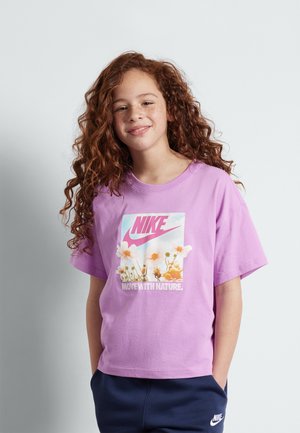 Camiseta de algodón morada con un gráfico de flor y el logo "Nike" en rosa, con mangas cortas y corte relajado. Combinada con pantalones en azul marino.