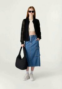 Μαύρο bomber μπουφάν με δαντελένιες λεπτομέρειες, λευκό crop τοπ, μπλε denim midi φούστα με τσέπη cargo, μαύρη τσάντα ώμου και λευκά sneakers.