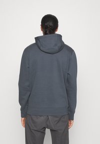 Sudadera con capucha en gris oscuro, con un corte holgado, puños de canalé y un bolsillo tipo canguro. Textura suave con detalles de costura visibles.