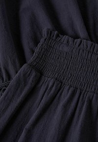 Tissu bleu marine avec une apparence texturée et froissée. Comprend des détails de smocks élastiques froncés à la taille pour un ajustement.
