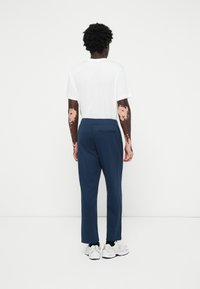 Pantaloni bleumarin cu un design drept, asociați cu un tricou alb. Buzunar vizibil la spate, completat cu pantofi sport albi.