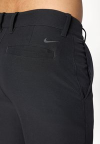 Sorte træningsbukser med en glat tekstur, der har sidelommer, en baglomme og et diskret Nike-logo på taljen.
