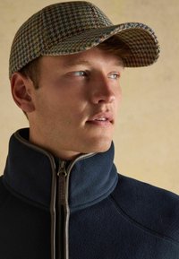 Villane müts, millel on sinise, kollase ja punase tooni houndstooth muster; tumesinine flleecejope kõrge kaelusega ja lukuga detailidega.