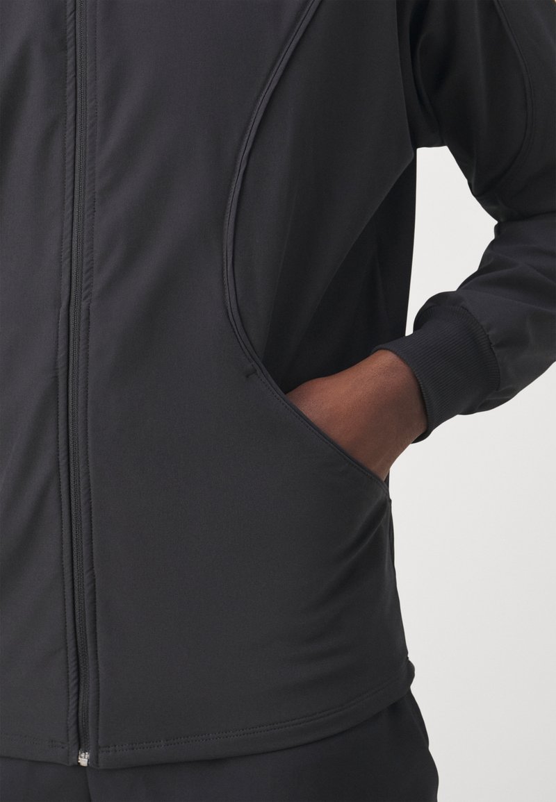 Zwarte sportieve zip-up jacket met een zachte textuur, zijzakken en ribgebreide boorden. Glad materiaal met een lichaamsscimiterend ontwerp.
