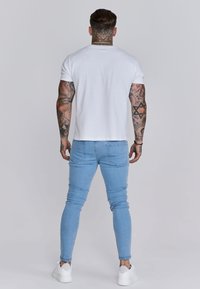 Vitt bomullströja i kombination med ljusblå smala jeans. Har en avslappnad passform och minimalistisk design, med subtila sömdetaljer och bakfickor.