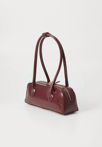 Sac à main en cuir bordeaux au design structuré, avec des poignées doubles et une fermeture éclair dorée. Texture lisse avec des détails matériels minimaux.