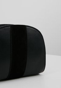 Borsa in pelle nera con finitura liscia e una striscia in suede a contrasto. Forma curva con dettagli di cucitura visibili.