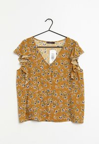 Mosterdgele blouse met een v-hals en geribbelde mouwen, met een bloemenpatroon in verschillende kleuren en subtiele verticale strepen.