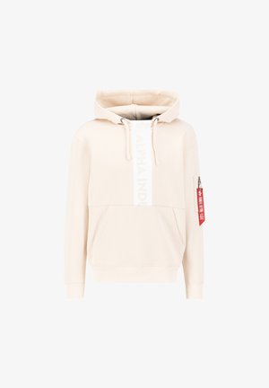 Cream-colored hoodie with front kangaroo pocket, vertical "Alpha Industries" text, drawstrings, and a small zip pocket with red "Remove Before Flight" tag on sleeve.