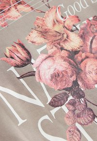Textil din țesătură ce prezintă un model floral cu trandafiri roz și lalele pe un fundal texturat bej. Litere albe parțial vizibile.