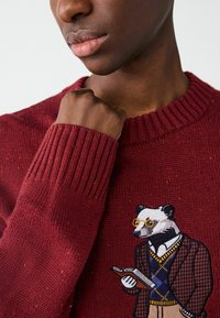 Burgundowy sweter z dzianiny z prążkowanymi mankietami. Wyjątkowy, duży haftowany borsuk w okularach, trzymający książkę, ubrany w marynarkę i kamizelkę.