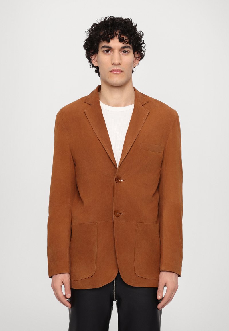 Brown suede blazer with two buttons, lapel collar, two front pockets, and a textured finish. Worn over a white undershirt.