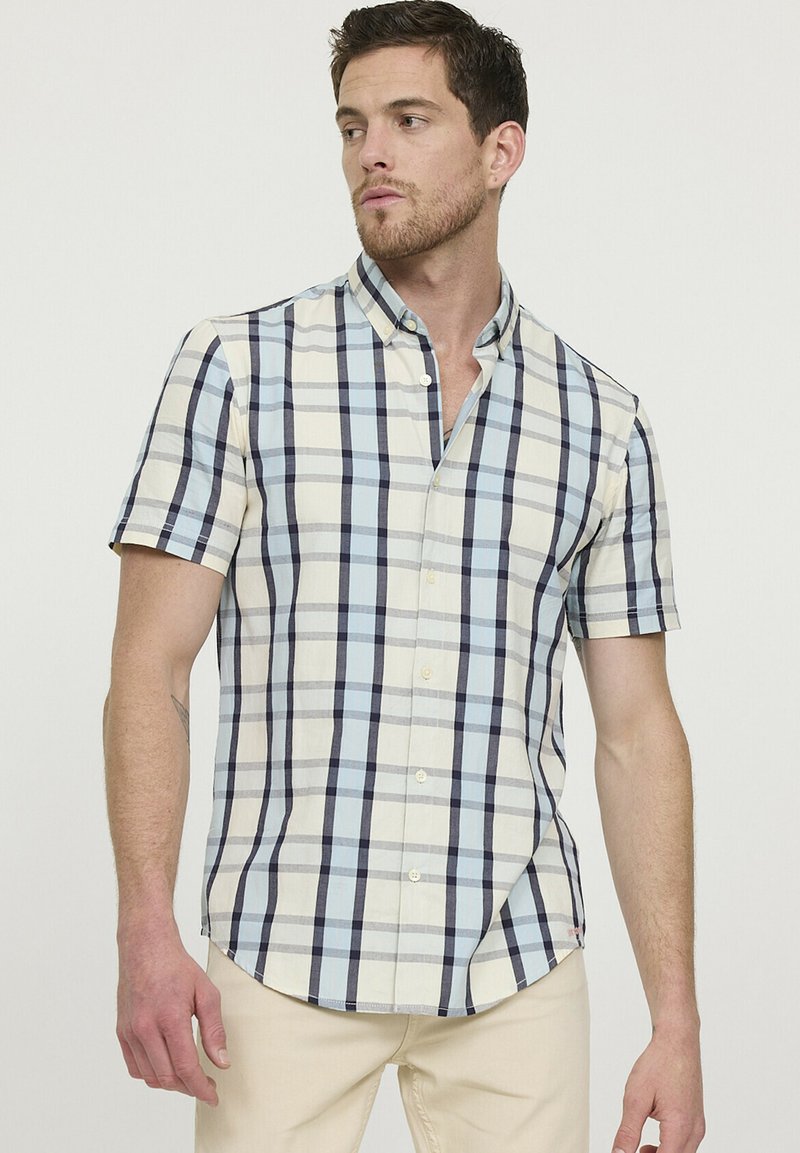 Chemise à manches courtes à carreaux dans des tons crème, bleu clair et marine. Présente un col à boutons et un ourlet arrondi. Matériau en coton avec une texture lisse.