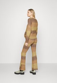 Conjunto de suéter e calças com um degradê de castanhos quentes e amarelos, textura tricotada, pernas alargadas e fendas laterais na bainha.
