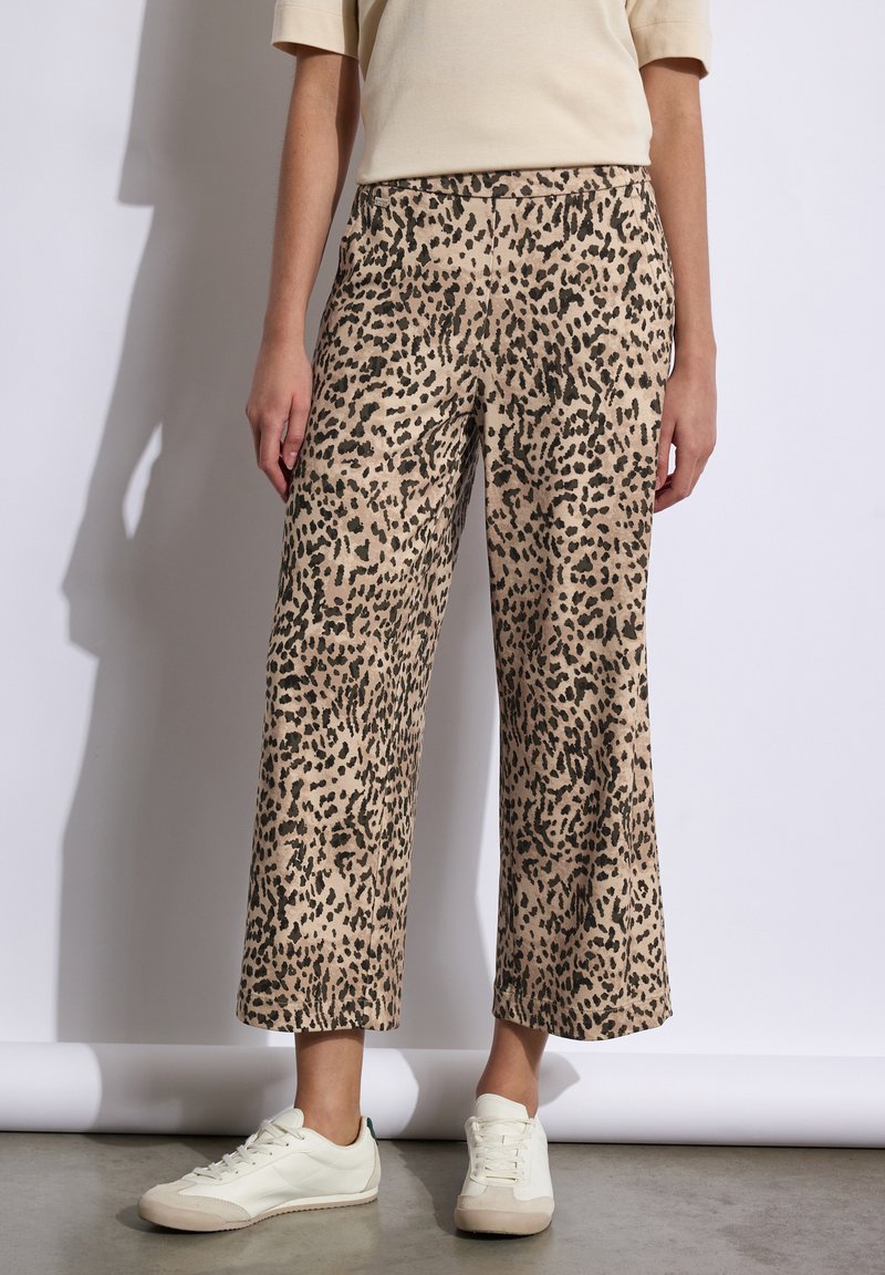 Pantalons large à imprimé léopard beige et noir, avec une texture de tissu douce et une taille élastique, associés à des baskets blanches.