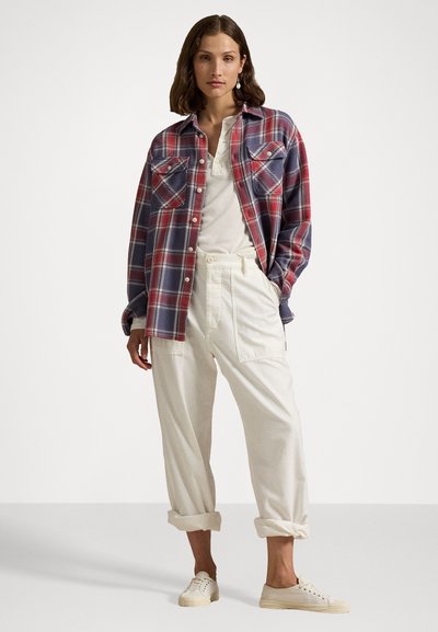 Plaid flannel shirt in blue and red; long sleeves, button-up front, two chest pockets. Paired with cream-colored, loose-fit trousers and sneakers.