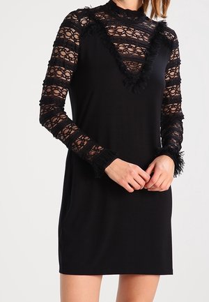 Black sleeveless dress with long sheer lace sleeves and high neckline, featuring ruffled trim on neckline and cuffs.