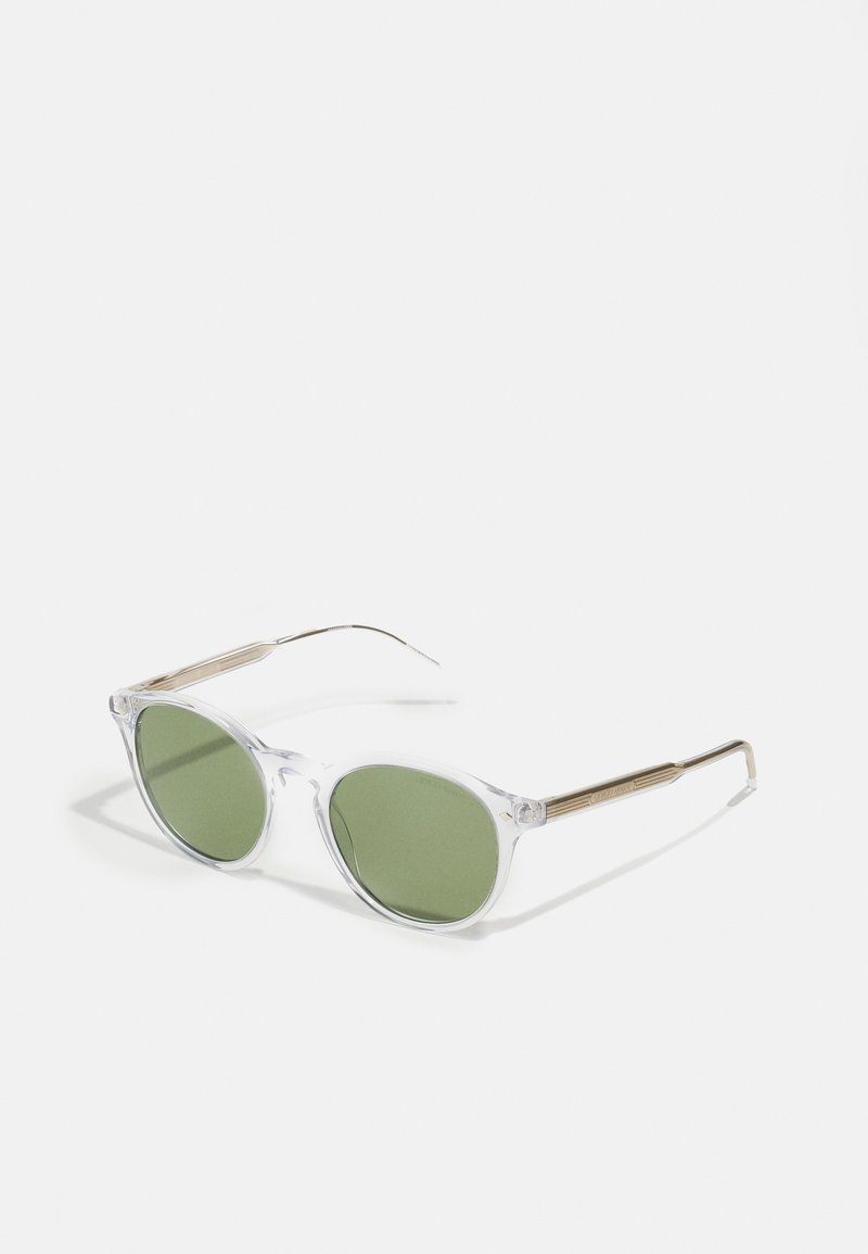Ochelari de soare cu ramă din plastic transparent, cu lentile verzi, accente din metal de culoare aurie și brațe, având lentile rotunde și o textură netedă.
