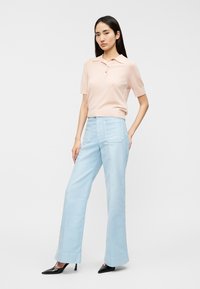 Ροζ ανοιχτόχρωμο polo με κοντά μανίκια και γιακά, σε συνδυασμό με ανοιχτό μπλε παντελόνια φαρδιάς γραμμής. Μαύρες μυτερές γόβες ολοκληρώνουν το σύνολο.