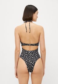 Schwarzer Badeanzug mit floralem Druck, Halter-Design, offenem Rücken und hoch geschnittenen Beinen. Verstellbare Bänder und ein Metallverschluss.