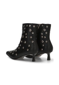 Botines de cuero negro con punta afilada, adornados con detalles plateados de ojetes y un tacón corto tipo kitten. Cierre con cremallera en la parte posterior.