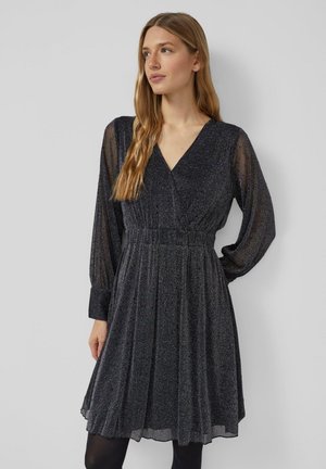 Zwarte sprankelende jurk met lange doorschijnende mouwen, diepe V-hals en geplooide taille. De rok is uitlopend, gemaakt van een vloeiende, gestructureerde stof.