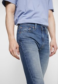 Bleka blå jeans i denim med en figursydd design, som har orange sömmar, femfickorsstil och bälteshällor i midjan. Mjuk textur.