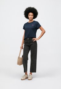 Ναυτικό βαμβακερό t-shirt με κοντά μανίκια και κεντημένο λογότυπο, συνδυασμένο με ψηλόμεσο, σκούρο γκρι παντελόνι φαρδιάς γραμμής και μπεζ αθλητικά παπούτσια.