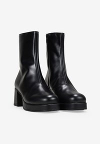 Botas de tobillo de cuero negro con un diseño elegante, punta redonda y tacón cuadrado. Cuentan con una cremallera lateral y una textura suave.
