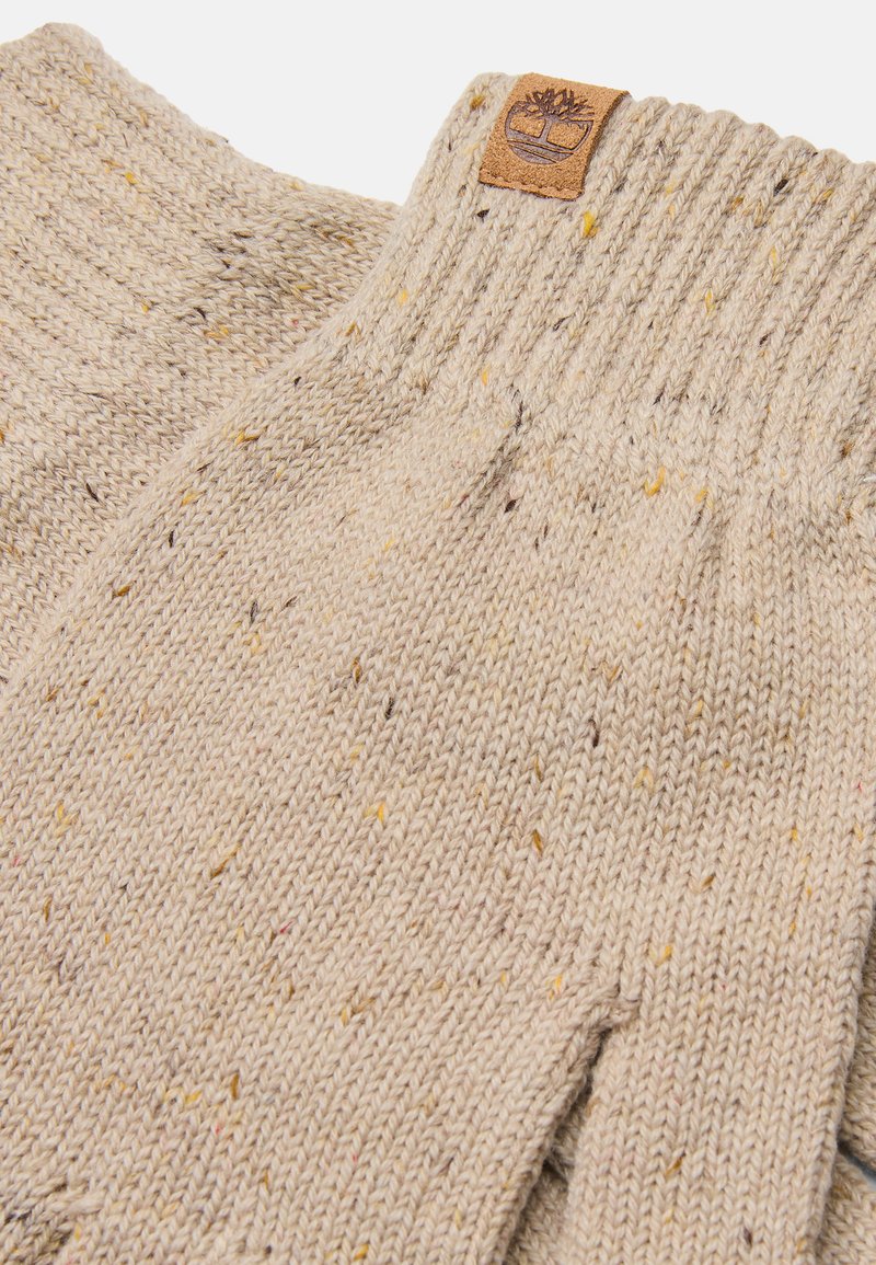 Beige gebreide handschoenen met gemêleerde patronen. Voorzien van een ribbelmanchet en een leren patch met logo. Zachte textuur, warme uitstraling.