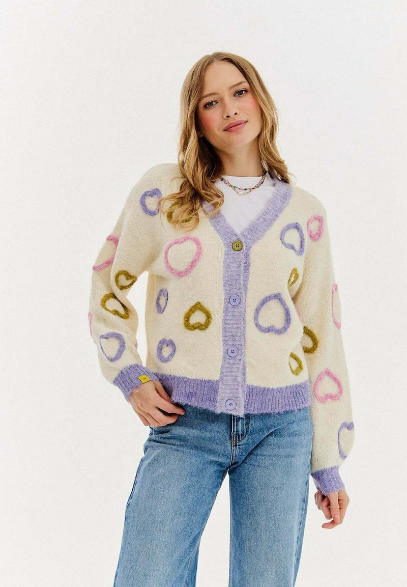 Krémový cardigan s vícebarevnými srdíčky, který má jemnou texturu, fialový lem a čtyři knoflíky vpředu. Vhodný pro neformální nošení.