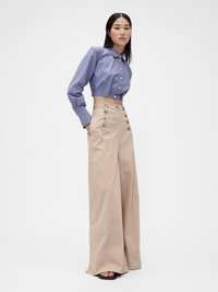 Camicia abbottonata a righe blu e bianche, corta e con colletto, abbinata a pantaloni ampi a vita alta beige con bottoni decorativi.