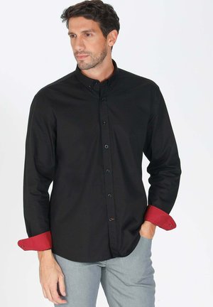 Chemise noire à manches longues avec un col boutonné, présentant des poignets contrastants rouges et des boutons noirs, accompagnée d'une coupe droite.