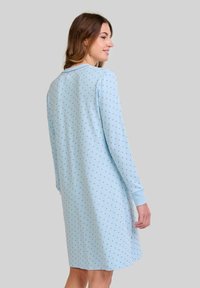 Camisa de noche azul claro con mangas largas, con un patrón de puntos en azul más oscuro. Fabricada en tejido suave, tiene un corte relajado y puños acanalados.