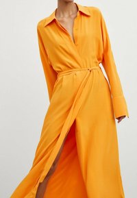 Orange Langarmhemdkleid mit Kragen, Wickeldesign und einer gebundenen Taillenbetonung. Glattes Material mit einem seitlichen Schlitz.