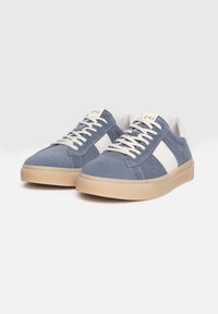 Zapatillas de ante azul con una franja blanca, cordones cremosos y una suela de goma beige con un acabado texturizado.
