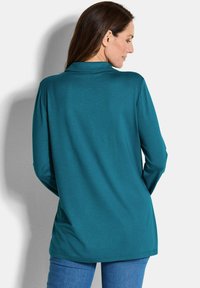 Tiefblaues Langarm-Shirt mit Kragen und lockerer Passform. Weicher Stoff, schlichte Gestaltung, keine Muster, kombiniert mit blauen Jeans.
