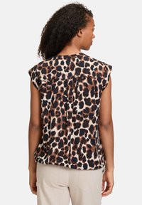 Top senza maniche marrone e crema con stampa leopardata, dotato di plissettature sul retro e vestibilità comoda, abbinato a pantaloni beige chiaro.