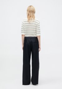 Striped knit top with short sleeves in cream, paired with high-waisted, wide-leg navy trousers. Features vertical and horizontal patterns.